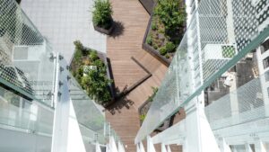 Vue plongeante sur la terrasse extérieure géométrique avec terrasse en bois, jardinières vertes luxuriantes et balustrades en verre modernes.